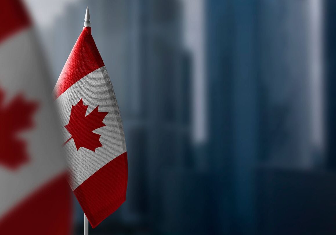 Canadian flag with blurred cityscape background.