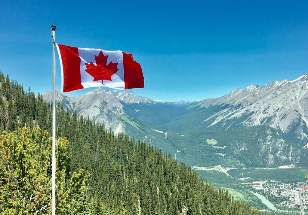 Canadian flag with mountainous landscape background.
